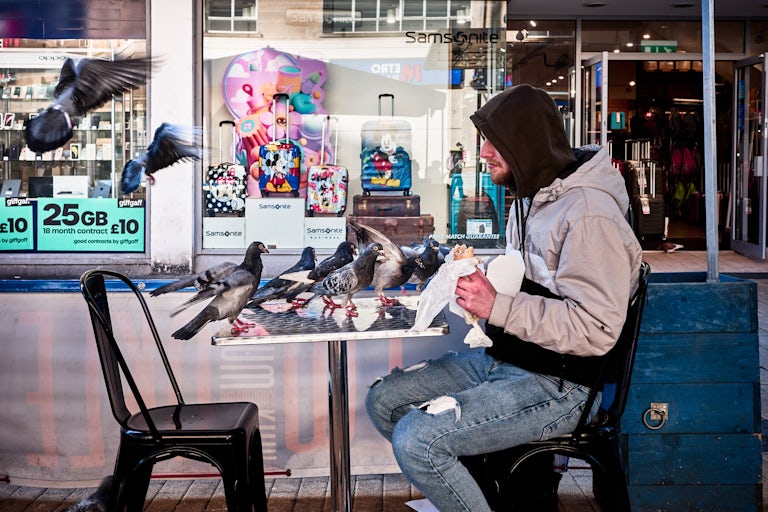 Mohamad having lunch with the pigeons, Broadmead, Bristol, January 2024. Photograph Copyright © Simon Holliday